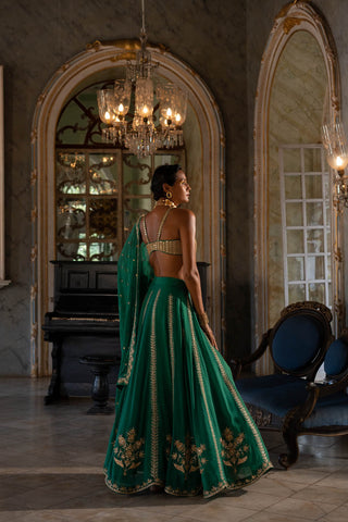 Model posing to show the side of the emerald green blouse and lehenga with dupatta.