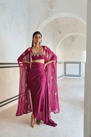 Magenta floral embroidered bralet with detailed neckline, paired with a matching floral butti embroidered jacket and draped cowl skirt, perfect for festive or ethnic fusion occasions. Designed by Ease.