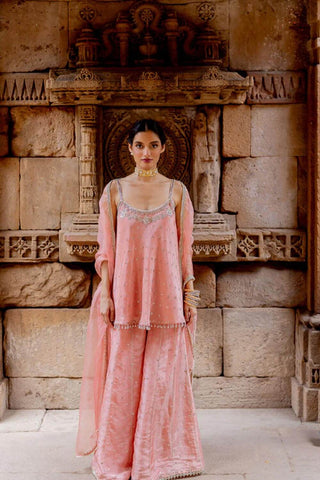 Featuring a rose pink flared top, hand embroidered with resham, dori, sequins and pearls in zari tissue base. It has a fit n flare look with noodle straps at the shoulder. Sleeves can be added on request. It comes with a matching sequins embroidered sharara in zari tissue base and a rose pink silk organza dupatta with lace edgings. Designer - Ivory By Dipika