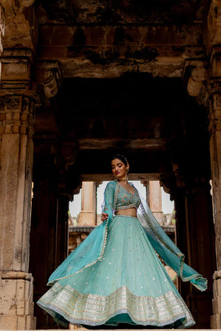 Featuring a sky blue embroidered flared lehenga in zari tissue base with zari, pearls and sequins embroidered thick border. It is paired with a matching hand embroidered blouse in tissue base with deep V-neckline and elbow length sleeves. It comes with a sky blue coloured silk organza dupatta with gota lace border on all sides. Designer - Ivory by Dipika
