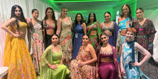 A group of twelve women posing together with Leela Lane founder in a hallway, showcasing a variety of colorful traditional Indian and indo-western outfits including sarees, lehengas, and western dresses with jacket sets in vibrant shades of yellow, green, pink, blue, and purple.