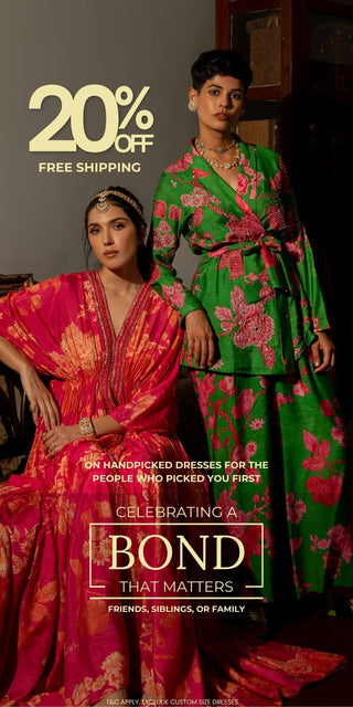 Two women modeling traditional Indian floral printed kurta sets in a dark indoor setting. One kurta is bright pink with gold embroidery, and the other is green co-ord set with pink floral print.