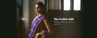 A woman in a purple and gold saree stands in a dimly lit interior doorway, with white promotional text on the right reading 'The Festive Edit' and 'Sarees, Ethnicwear, Dresses and more.