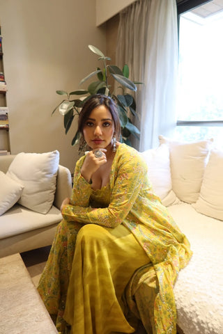 Neha Sharme wearing a yami Jacket set, embroidered traditional fusion outfit sits on a white sofa in a living room setting. In her me moment, posing soft, strong and self-assured look.