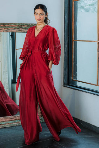 Model wearing a cherry red silk organza jumpsuit with intricate floral embroidery with deep v-neck and voluminous sleeves , styled for a formal evening party, cocktail parties, brunch to soiree. Designed by Paulmi and Harsh.