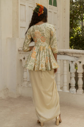 A woman photographed from behind wearing a traditional outfit with a floral peplum-style top and a flowing ivofry skirt, standing on a balcony in front of a white building.
