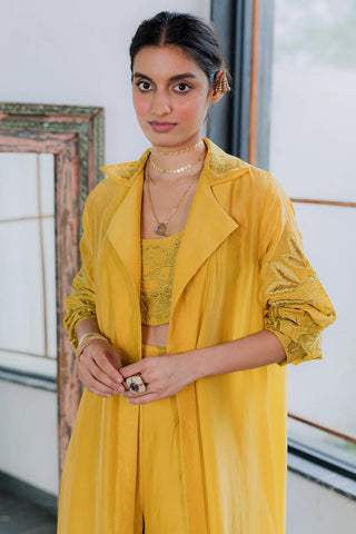 Model wearing long yellow jacket with matching blouse and trousers strewn with beautiful florals on the blouse and jacket, in delicate cutwork embroidery. 