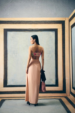 A woman stands with her back to the camera wearing a pink jacket dress with a floral strapless crop top. She is styling with a bag and high heels posing her back.
