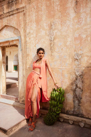A model posing in a resort look. The dress is in coral colour made from linen crop top, Linen jacket with cut work floral embroidery, silk organza warp pre-stitched skirt. A perfect resort look book dress, holiday, vacation, coastal, beach wear.