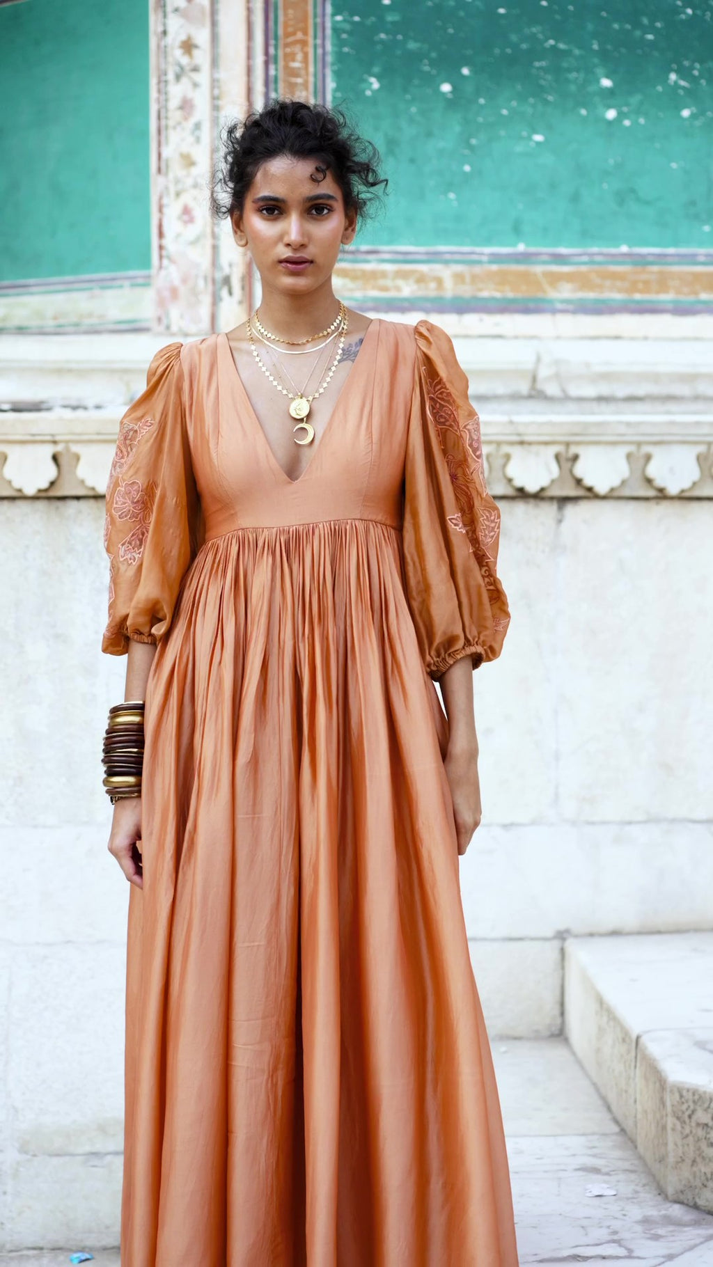 Model in peachy orange maxi dress crafted in a soft silk organza fabric. The dress has deep V neck and voluminous sleeves. The dress also features floral motif cutwork embroidery which makes it the perfect dress for a fancy brunch date. Designed by Paulmi and Harsh.