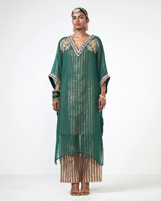 A woman models a green sheer kaftan kurta dress with gold and silver vertical stripes on organza, featuring embroidered detailing on the V-neckline and sleeve cuffs, paired with striped pants, against a plain white studio background.    Perfect style for wedding and festive occasions or events.